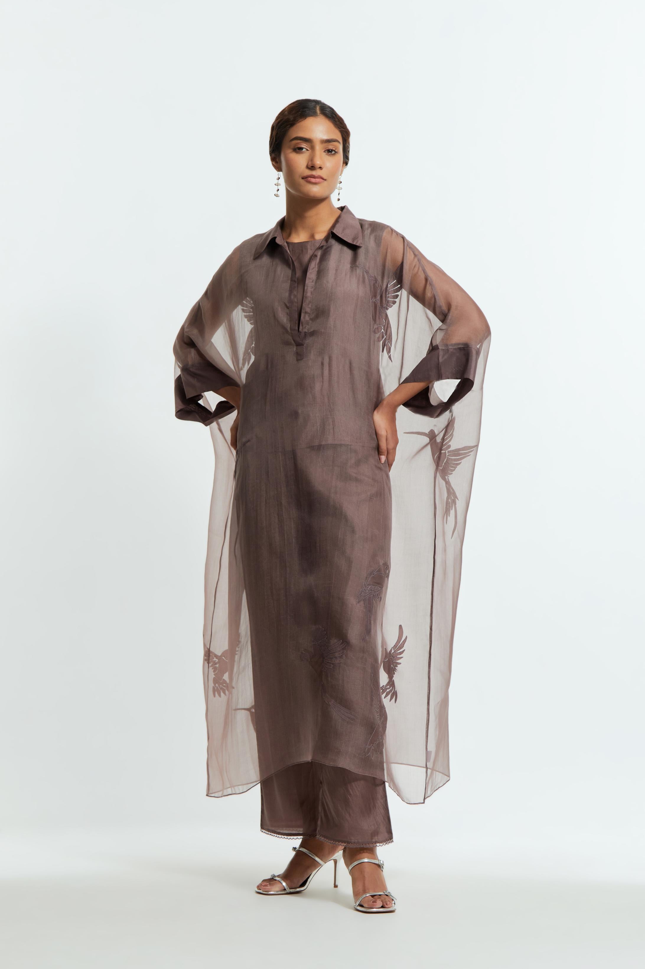 Grey silk organza kaftan with a sheer finish, delicately adorned with appliqué bird motifs along the hem and sides. Paired with Grey silk straight pants detailed with scalloped organza edging at the hem, delicately highlighted with tonal beadwork.