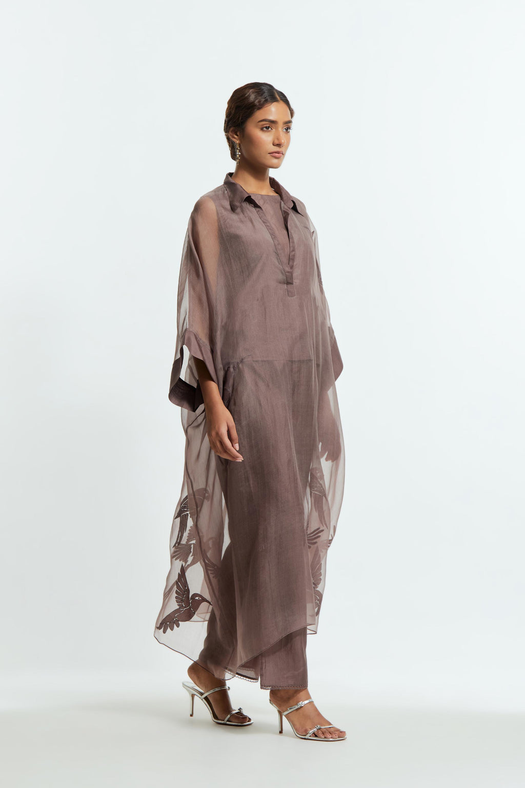 Grey silk organza kaftan with a sheer finish, delicately adorned with appliqué bird motifs along the hem and sides. Paired with Grey silk straight pants detailed with scalloped organza edging at the hem, delicately highlighted with tonal beadwork.