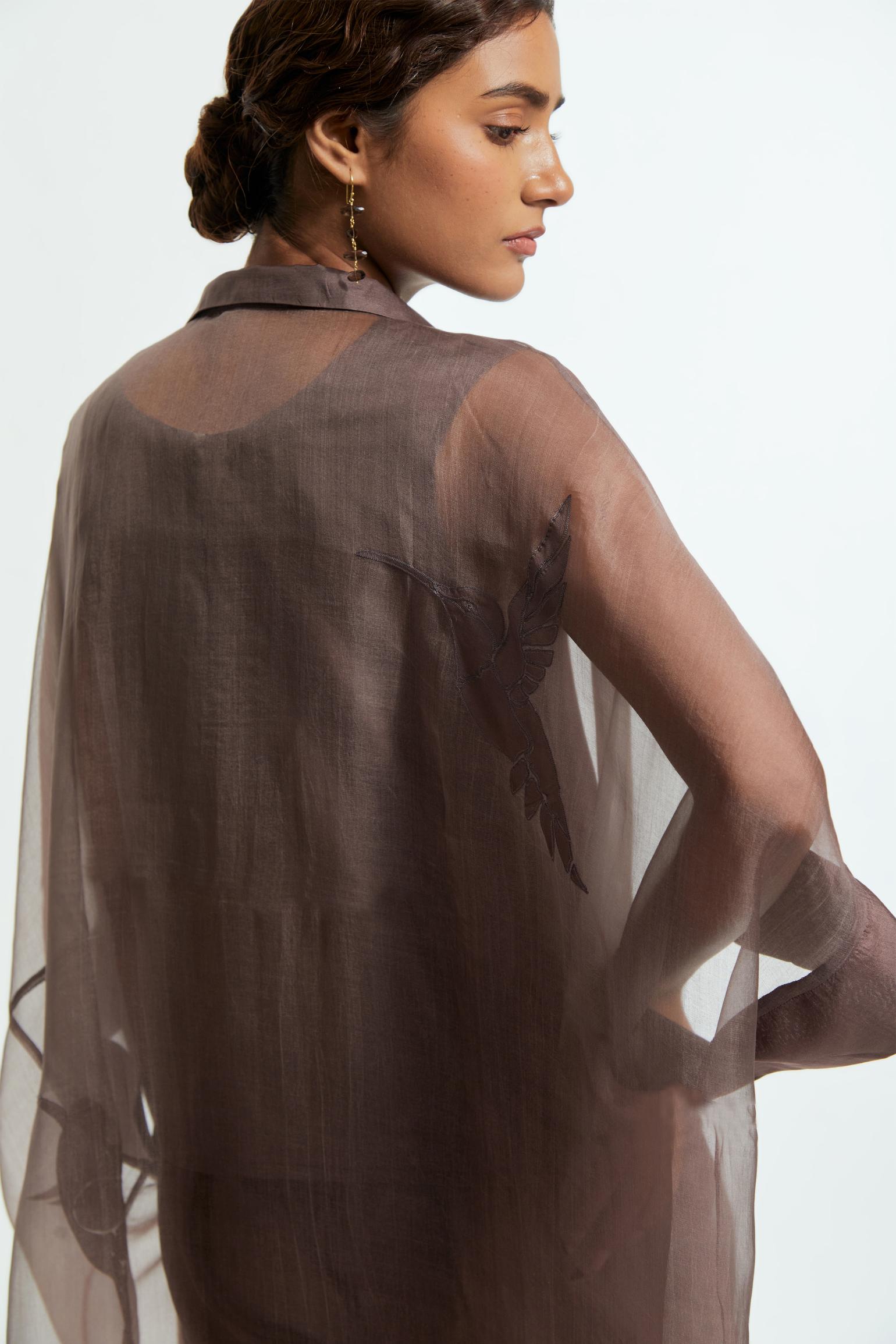 Grey silk organza kaftan with a sheer finish, delicately adorned with appliqué bird motifs along the hem and sides. Paired with Grey silk straight pants detailed with scalloped organza edging at the hem, delicately highlighted with tonal beadwork.