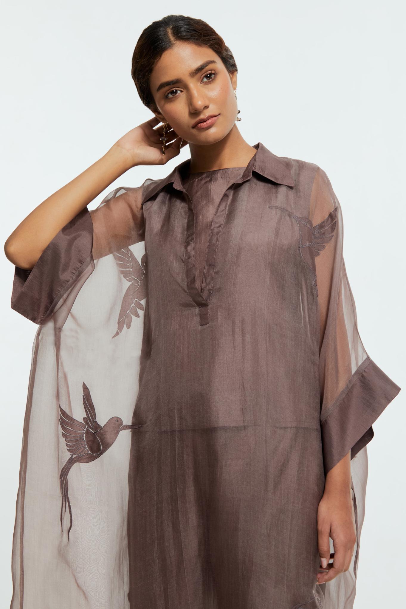 Grey silk organza kaftan with a sheer finish, delicately adorned with appliqué bird motifs along the hem and sides. Paired with Grey silk straight pants detailed with scalloped organza edging at the hem, delicately highlighted with tonal beadwork.