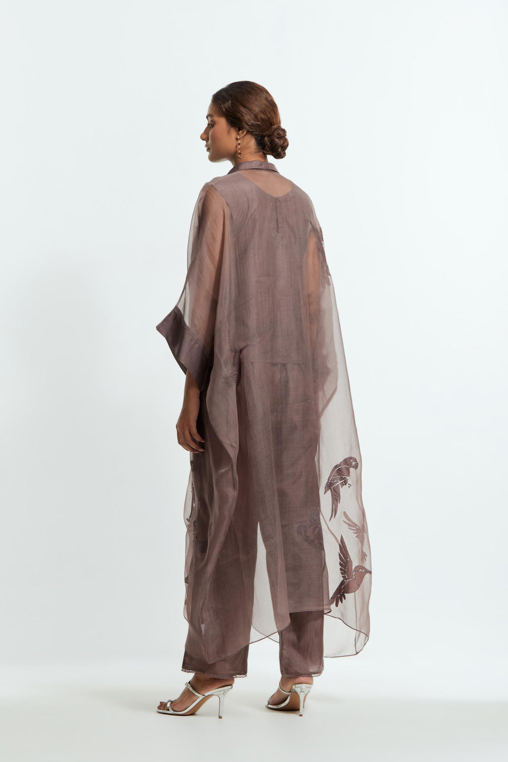 Grey silk organza kaftan with a sheer finish, delicately adorned with appliqué bird motifs along the hem and sides. Paired with Grey silk straight pants detailed with scalloped organza edging at the hem, delicately highlighted with tonal beadwork.