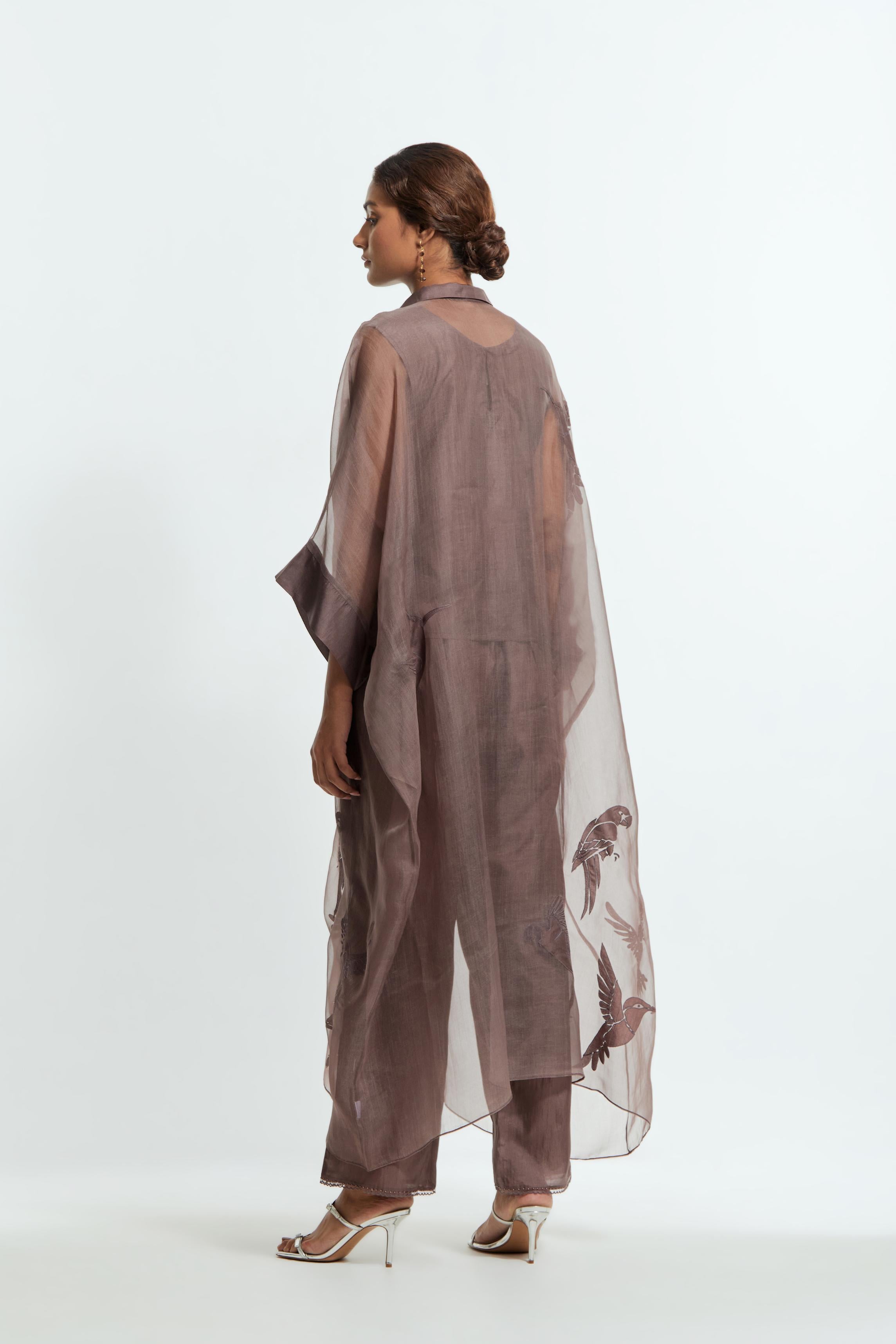 Grey silk organza kaftan with a sheer finish, delicately adorned with appliqué bird motifs along the hem and sides. Paired with Grey silk straight pants detailed with scalloped organza edging at the hem, delicately highlighted with tonal beadwork.