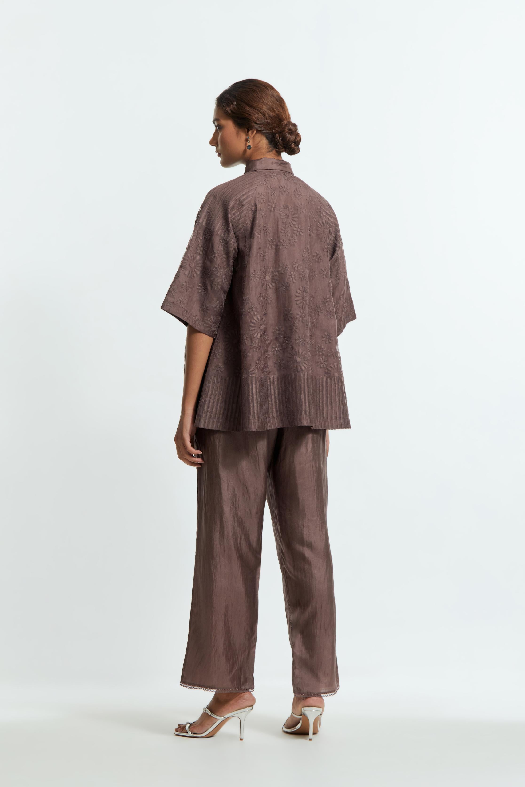 Grey silk organza short top featuring silk appliqué floral motifs and a shirt collar neckline. Paired with Grey silk straight pants detailed with scalloped organza edging at the hem, delicately highlighted with tonal beadwork.