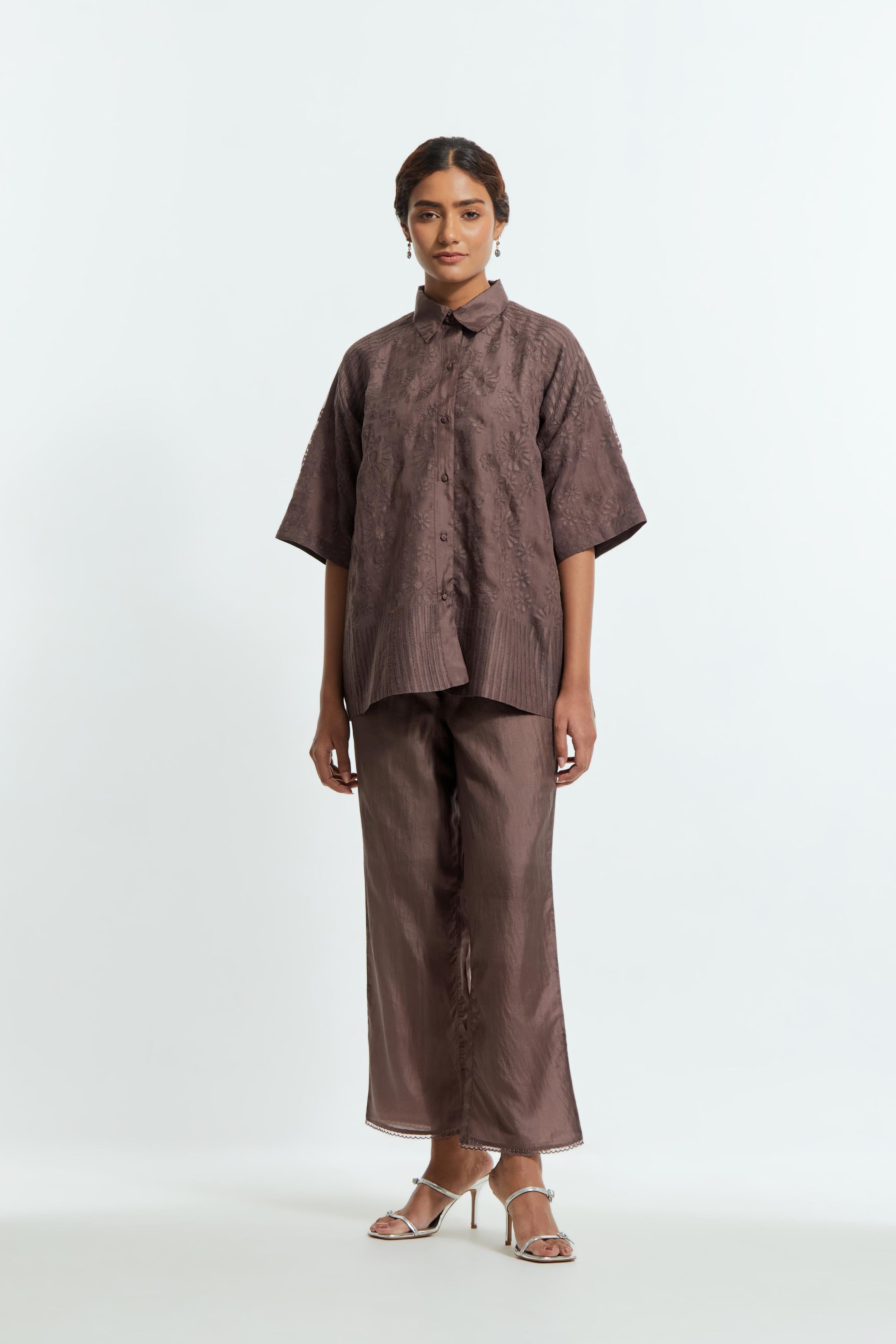 Grey silk organza short top featuring silk appliqué floral motifs and a shirt collar neckline. Paired with Grey silk straight pants detailed with scalloped organza edging at the hem, delicately highlighted with tonal beadwork.