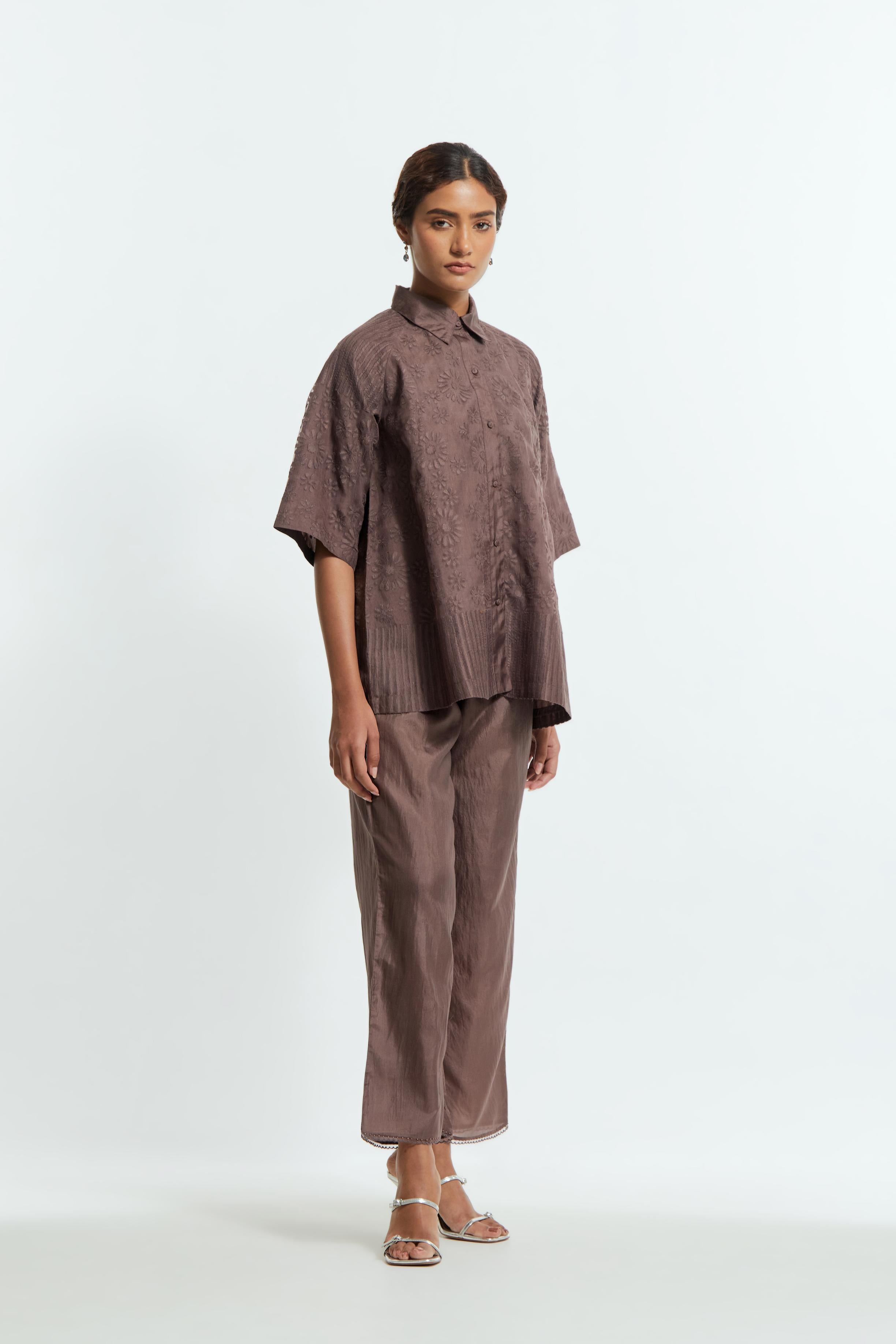 Grey silk organza short top featuring silk appliqué floral motifs and a shirt collar neckline. Paired with Grey silk straight pants detailed with scalloped organza edging at the hem, delicately highlighted with tonal beadwork.