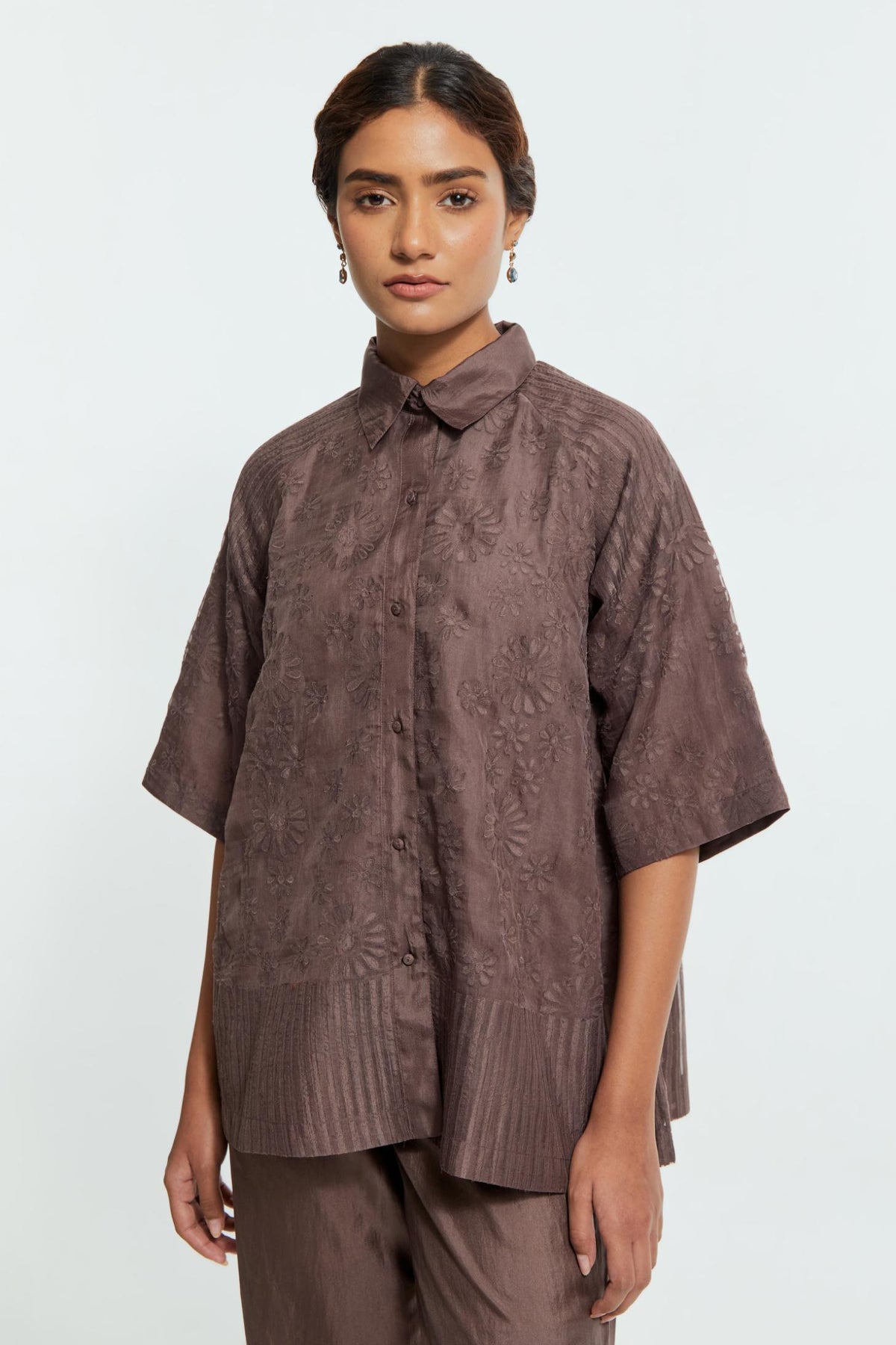 Grey silk organza short top featuring silk appliqué floral motifs and a shirt collar neckline. Paired with Grey silk straight pants detailed with scalloped organza edging at the hem, delicately highlighted with tonal beadwork.