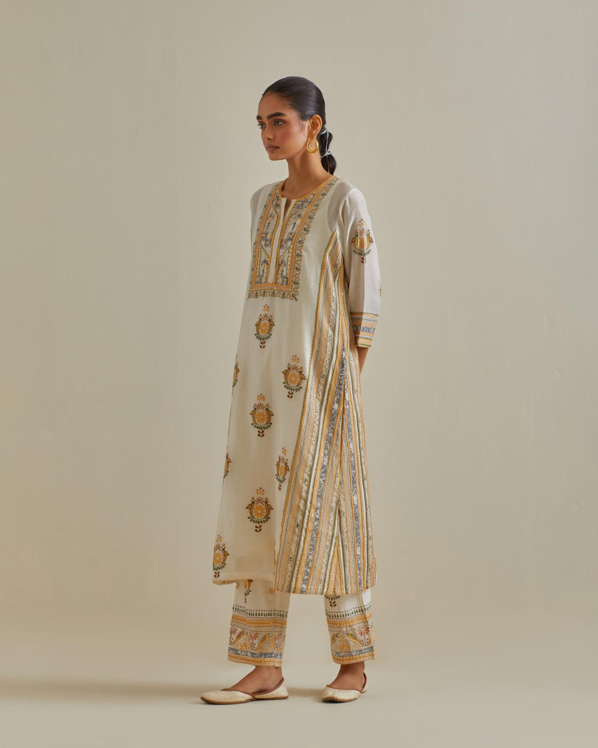 Yellow and off-white cotton chanderi straight kurta set with yoke and side panels. It has allover patchwork and silk thread embroidery, highlighted with mirror, sequins, tassels and braids.