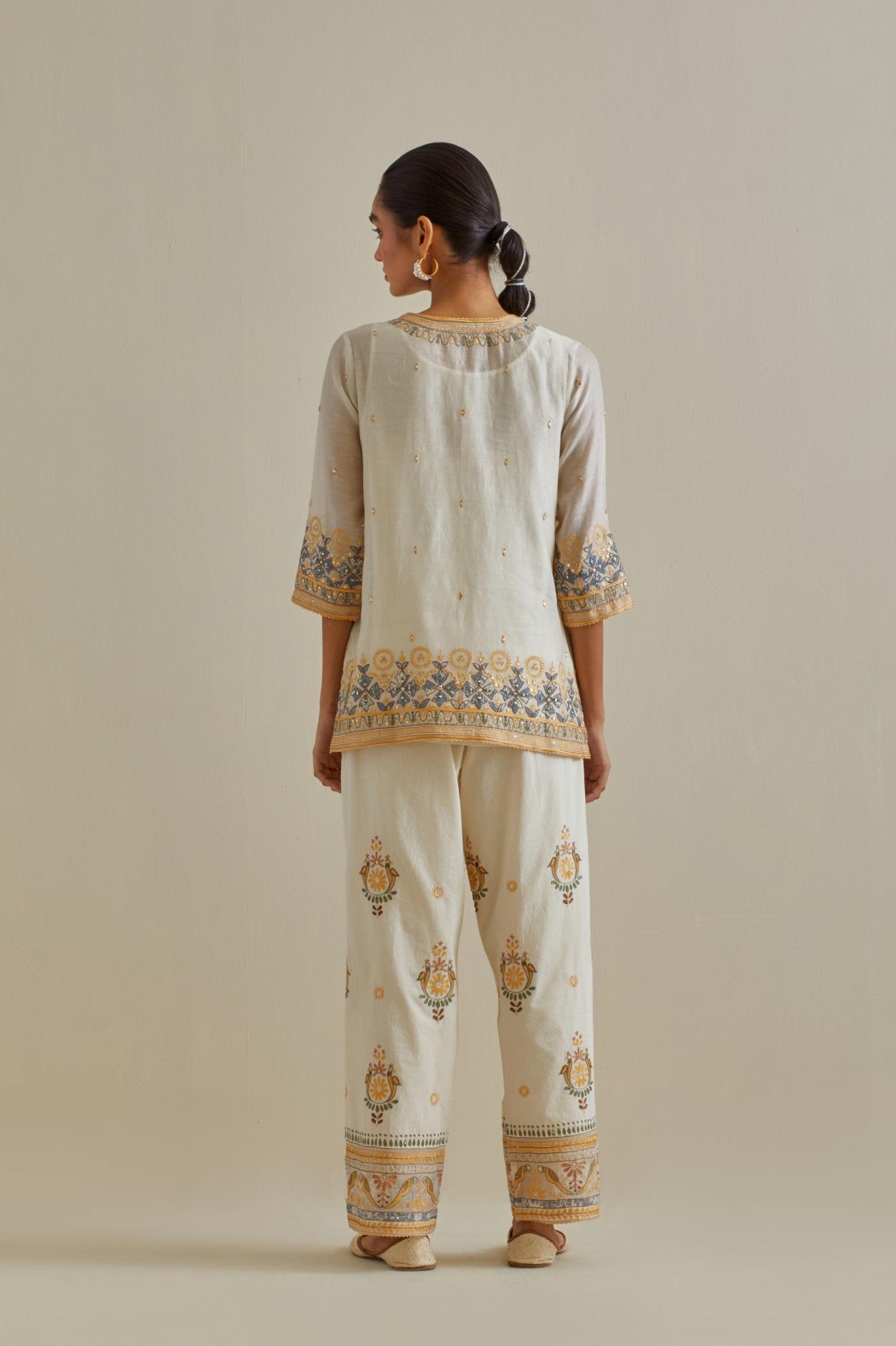 Yellow and off-white cotton chanderi embroidered short top with 3/4th sleeves, paired with off white cotton straight pants with all over multi color embroidery detailed with sequins.
