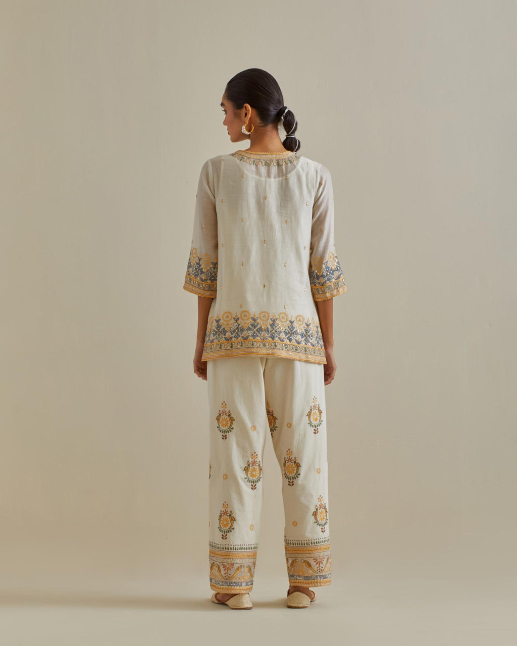 Yellow and off-white cotton chanderi embroidered short top with 3/4th sleeves, paired with off white cotton straight pants with all over multi color embroidery detailed with sequins.