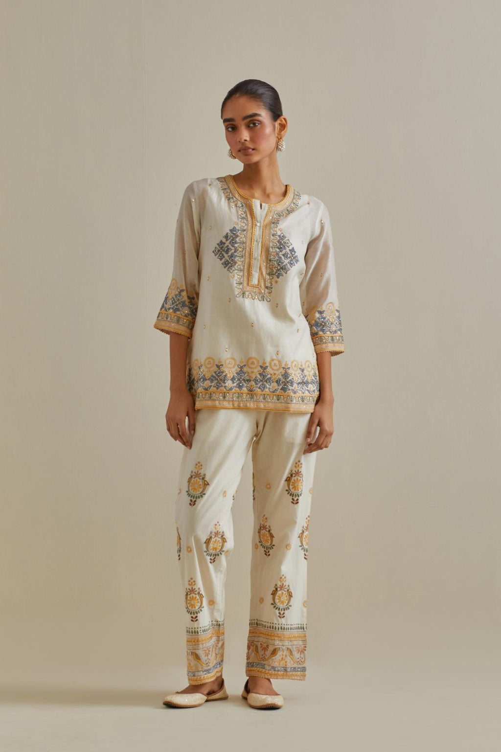 Yellow and off-white cotton chanderi embroidered short top with 3/4th sleeves, paired with off white cotton straight pants with all over multi color embroidery detailed with sequins.