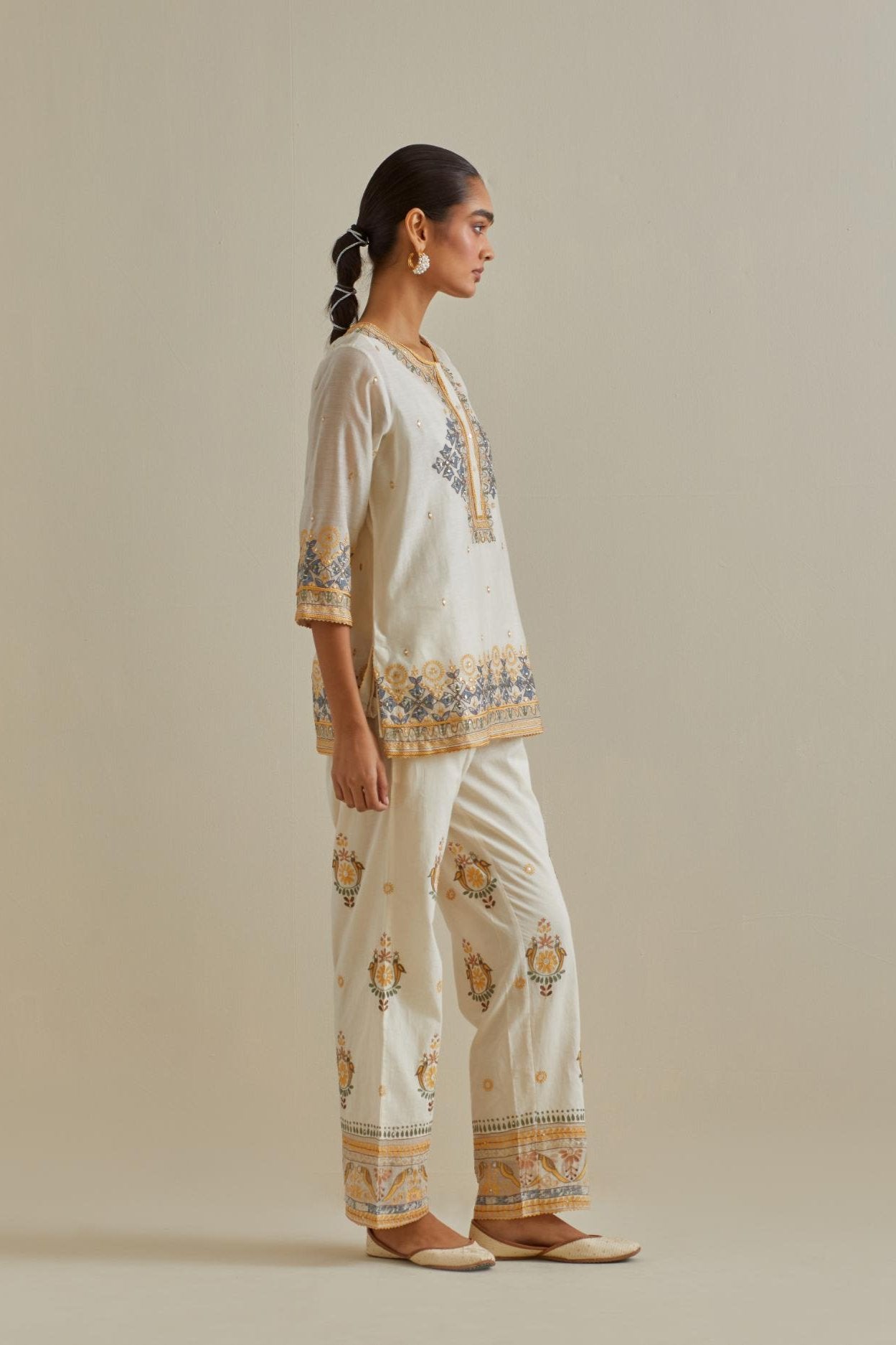 Yellow and off-white cotton chanderi embroidered short top with 3/4th sleeves, paired with off white cotton straight pants with all over multi color embroidery detailed with sequins.