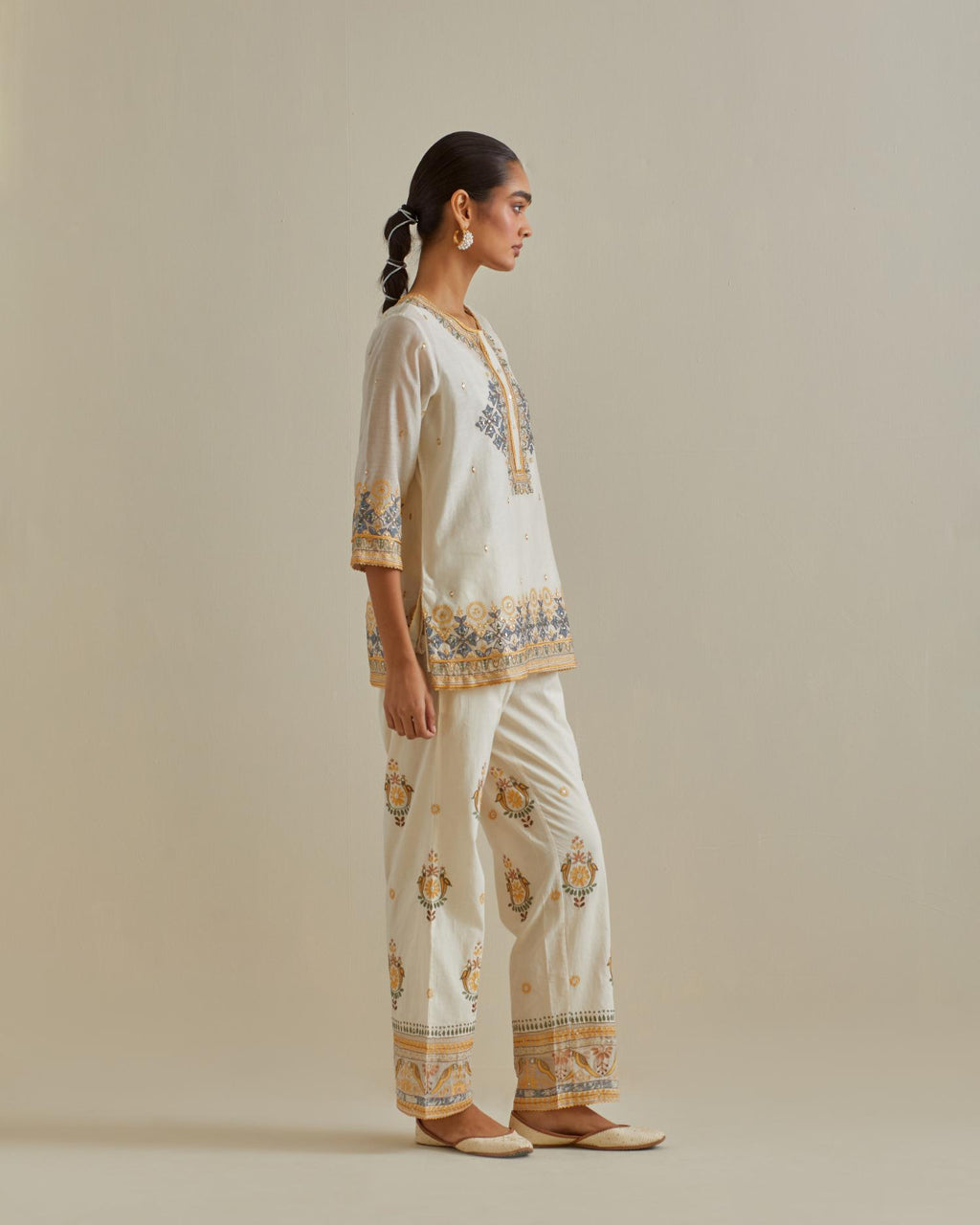 Yellow and off-white cotton chanderi embroidered short top with 3/4th sleeves, paired with off white cotton straight pants with all over multi color embroidery detailed with sequins.