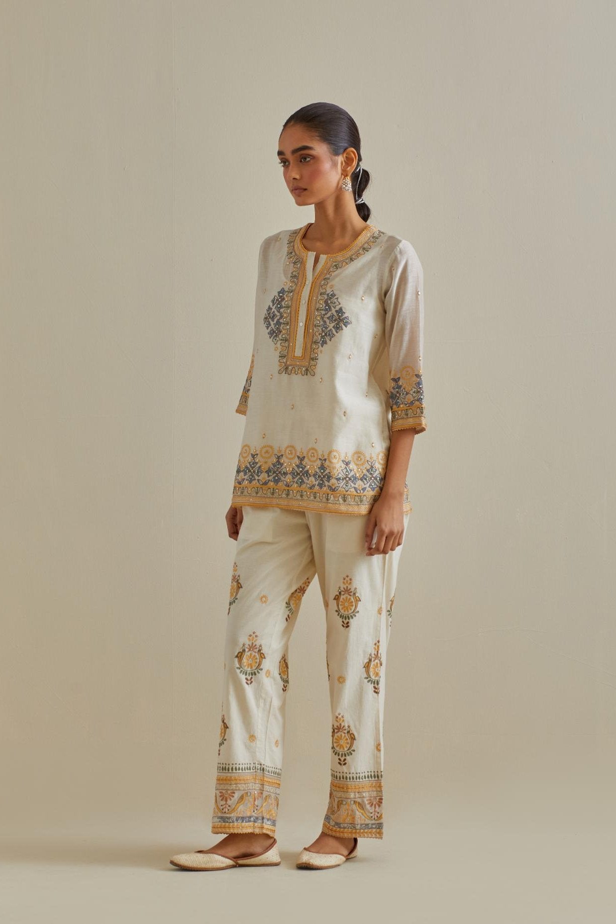 Yellow and off-white cotton chanderi embroidered short top with 3/4th sleeves, paired with off white cotton straight pants with all over multi color embroidery detailed with sequins.
