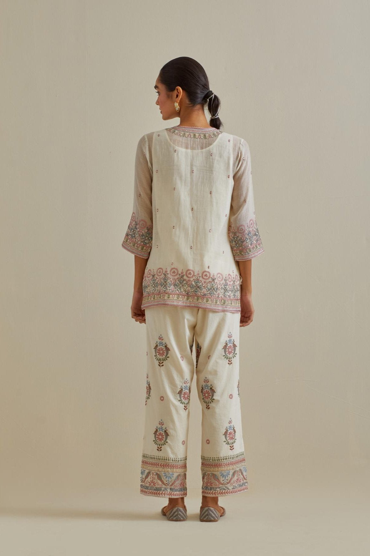 Pink and off-white cotton chanderi embroidered short top with 3/4th sleeves, paired with off white cotton straight pants with all over multi color embroidery detailed with sequins.