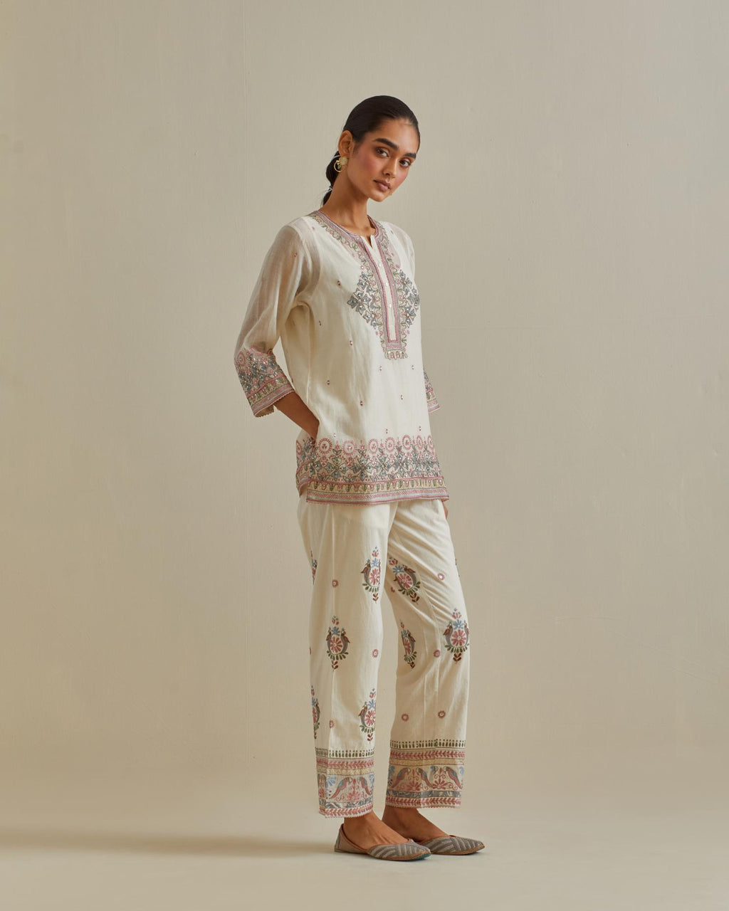 Pink and off-white cotton chanderi embroidered short top with 3/4th sleeves, paired with off white cotton straight pants with all over multi color embroidery detailed with sequins.