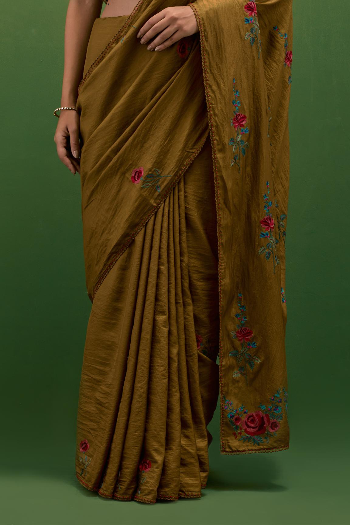 Golden olive silk saree with all-over thread embroidered roses and scalloped organza with delicate bead detail at the edges, paired with golden olive silk blouse with all-over pin tucks, highlighted with bead work.