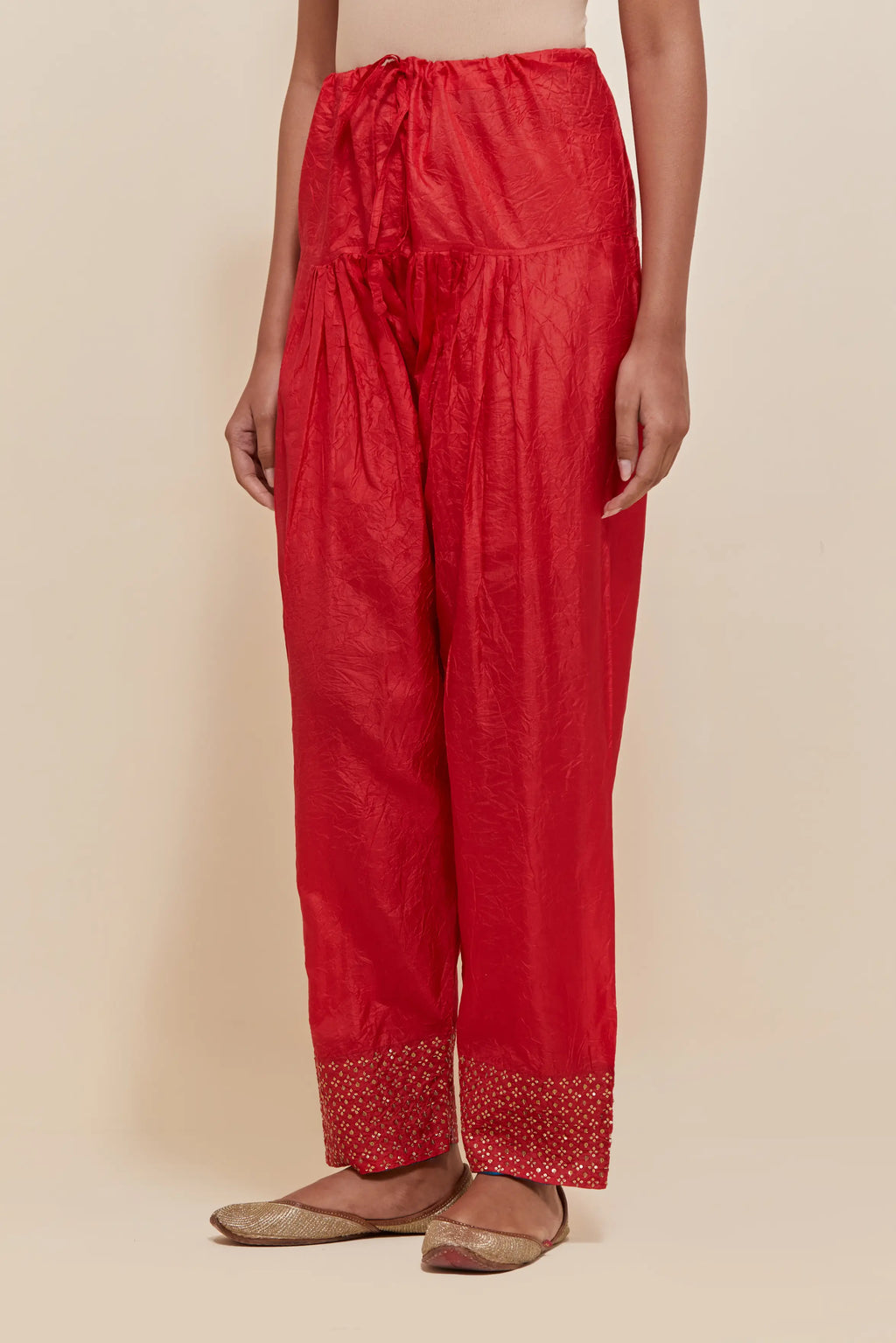 Red silk salwar with hand-embroidered gold sequin work in a broad border at the hem.