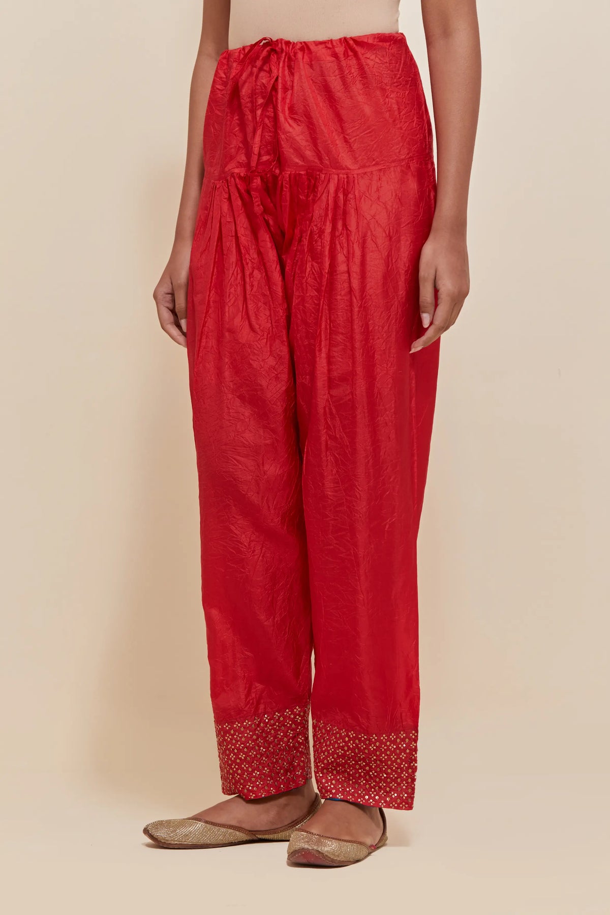 Red silk salwar with hand-embroidered gold sequin work in a broad border at the hem.
