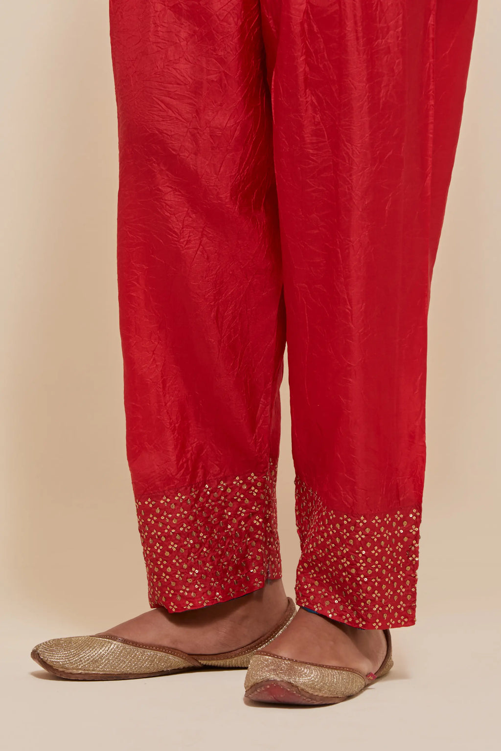 Red silk salwar with hand-embroidered gold sequin work in a broad border at the hem.