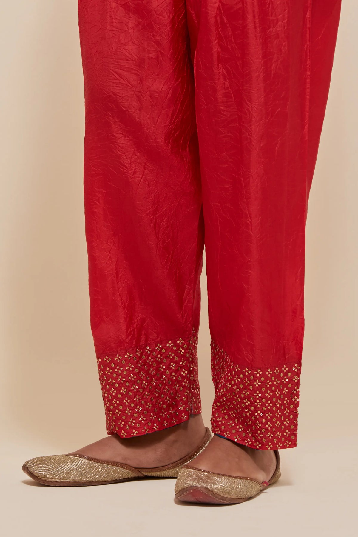 Red silk salwar with hand-embroidered gold sequin work in a broad border at the hem.