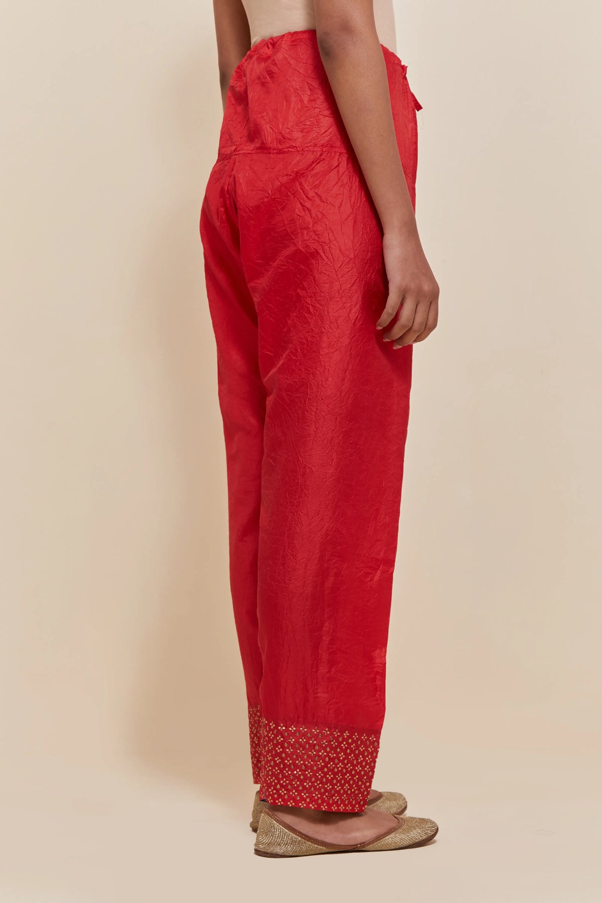 Red silk salwar with hand-embroidered gold sequin work in a broad border at the hem.