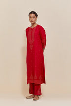 Red silk straight kurta set with hand-embroidered sequins at the neck, borders running along the hem and sleeve edges, and scattered gold sequins embellishments all-over.