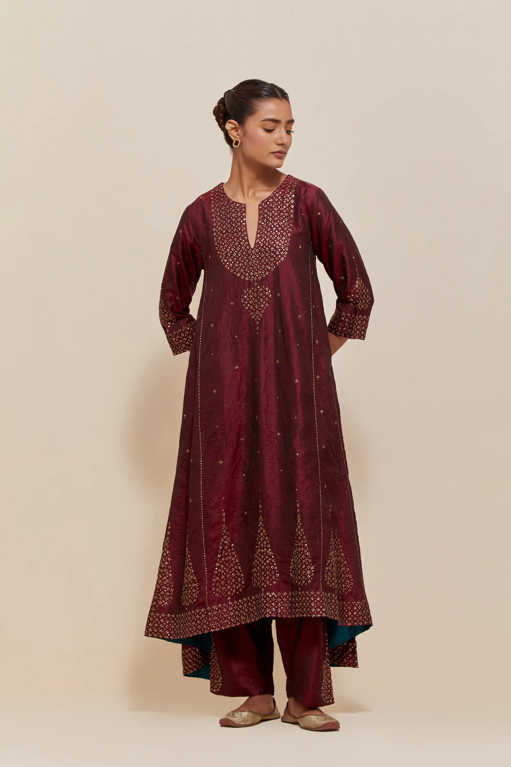 Maroon silk kurta set with asymmetric hem and hand-embroidered leaf motifs with delicate sequins work at the neck, sleeves, and hem, with sequins border running along the edges.