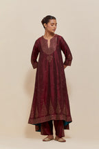 Maroon silk kurta set with asymmetric hem and hand-embroidered leaf motifs with delicate sequins work at the neck, sleeves, and hem, with sequins border running along the edges.