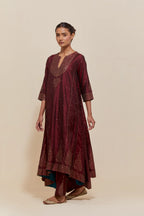 Maroon silk kurta set with asymmetric hem and hand-embroidered leaf motifs with delicate sequins work at the neck, sleeves, and hem, with sequins border running along the edges.