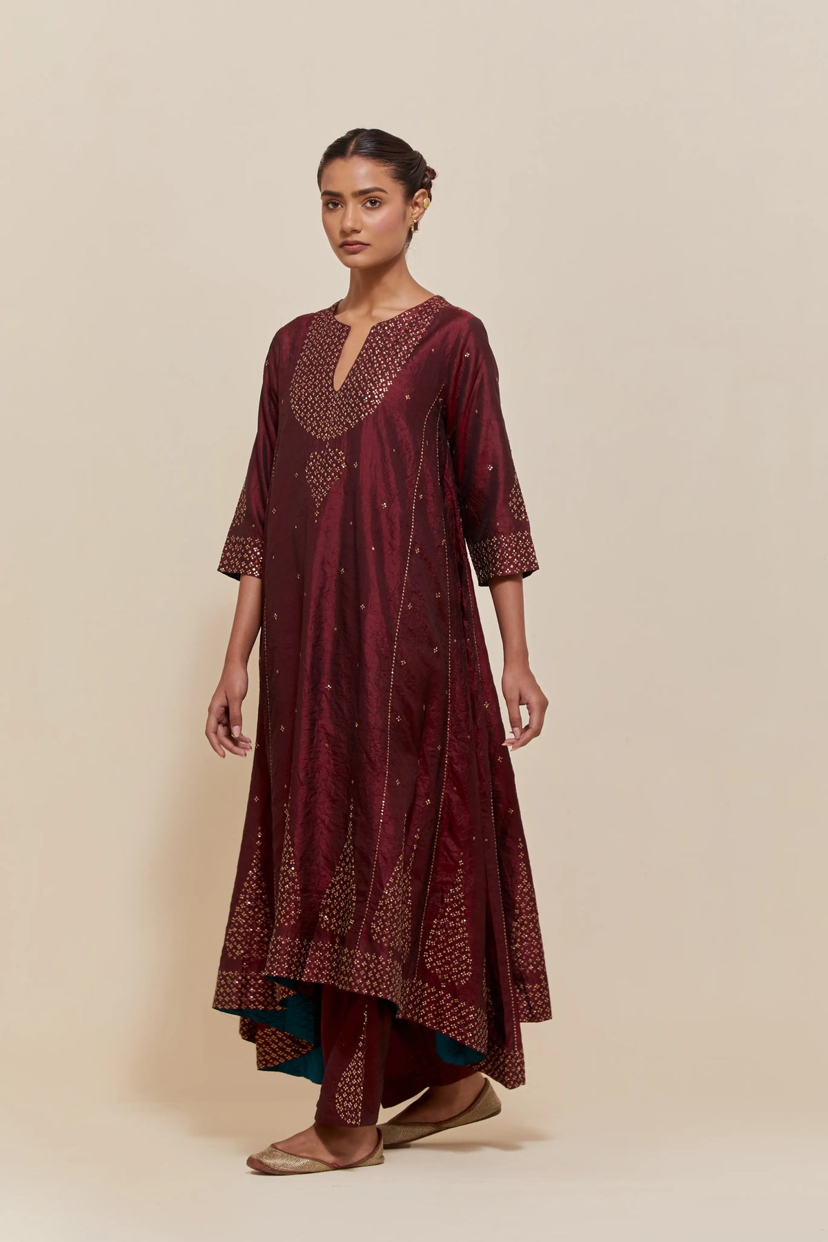 Maroon silk kurta set with asymmetric hem and hand-embroidered leaf motifs with delicate sequins work at the neck, sleeves, and hem, with sequins border running along the edges.