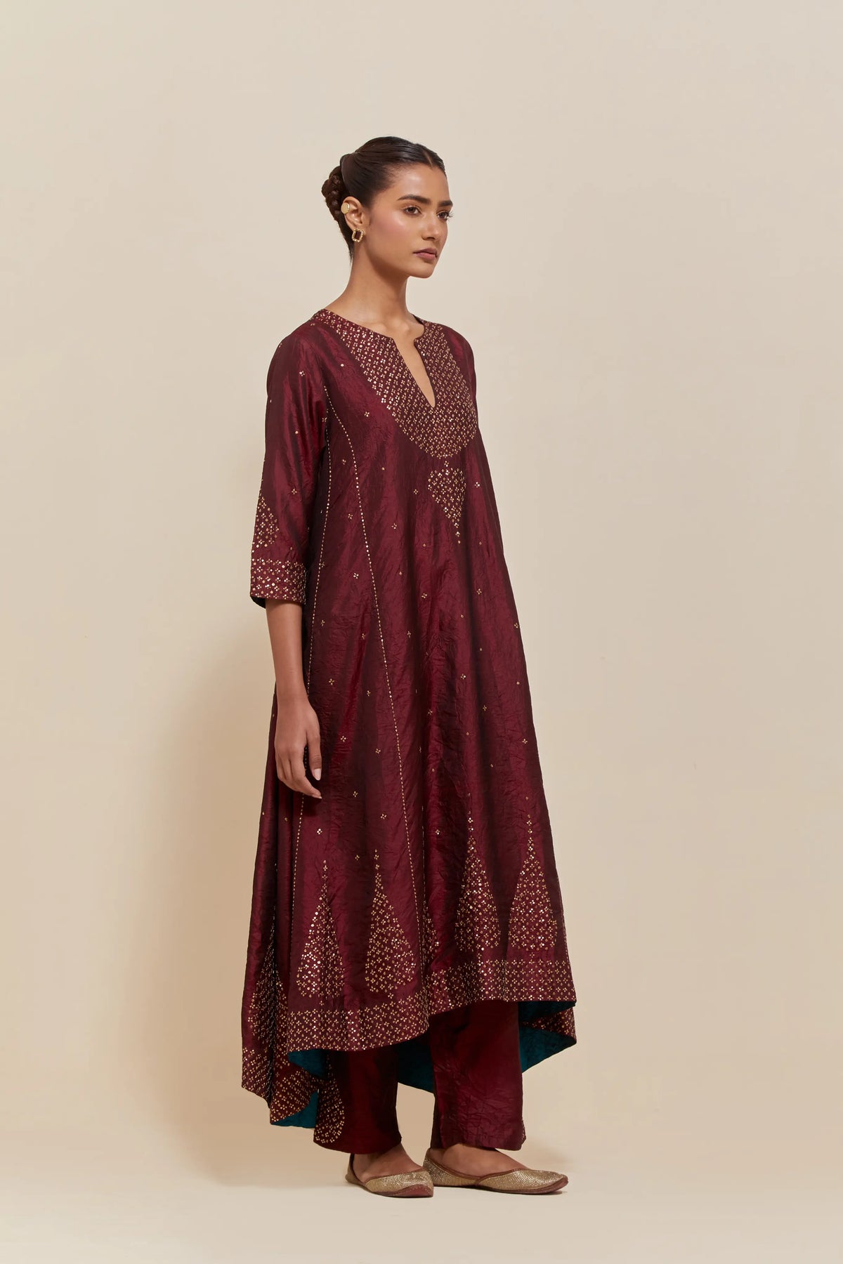Maroon silk kurta set with asymmetric hem and hand-embroidered leaf motifs with delicate sequins work at the neck, sleeves, and hem, with sequins border running along the edges.