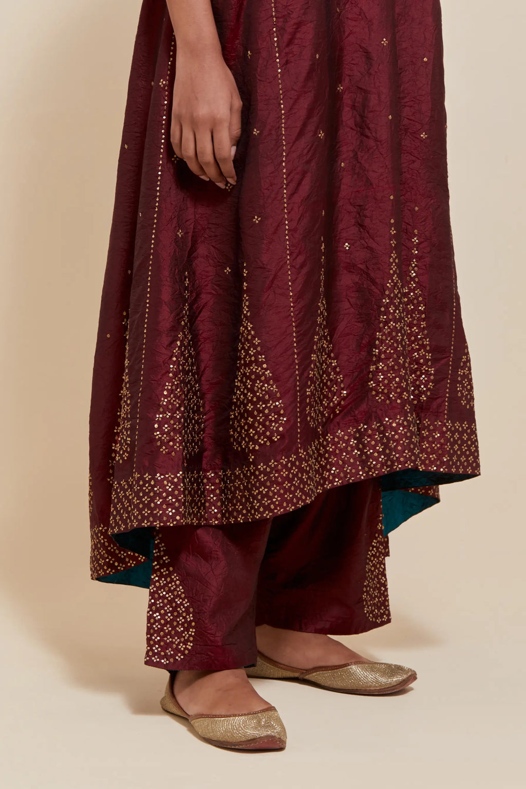 Maroon silk kurta set with asymmetric hem and hand-embroidered leaf motifs with delicate sequins work at the neck, sleeves, and hem, with sequins border running along the edges.