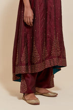 Maroon silk kurta set with asymmetric hem and hand-embroidered leaf motifs with delicate sequins work at the neck, sleeves, and hem, with sequins border running along the edges.