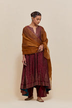 Maroon silk kurta set with asymmetric hem and hand-embroidered leaf motifs with delicate sequins work at the neck, sleeves, and hem, with sequins border running along the edges.