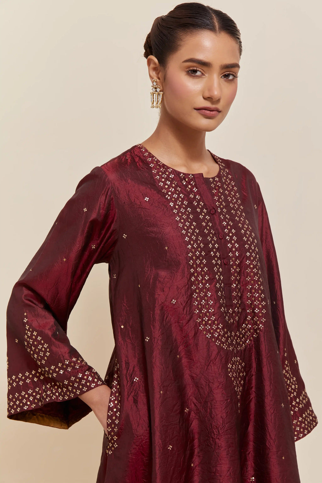 Maroon silk A-line short kurta set with hand-embroidered sequins at the neck, borders running along the hem and sleeve edges, and scattered gold sequin embellishments all-over.