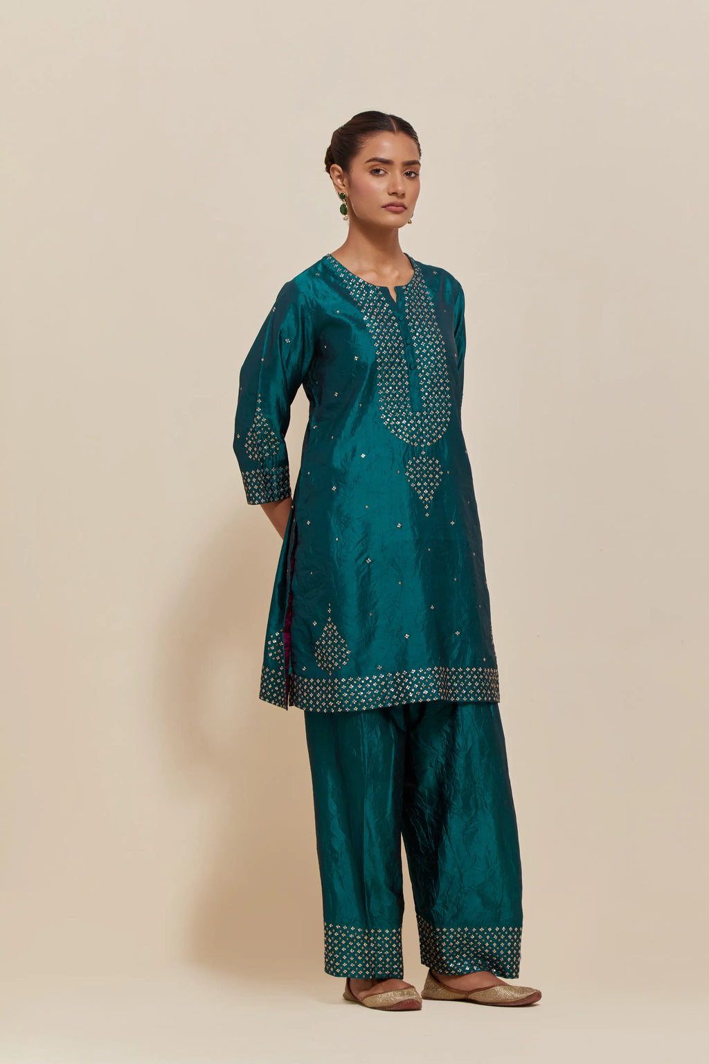 Teal green silk straight short kurta set with hand-embroidered sequins at the neck, borders running along the hem and sleeve edges, and scattered gold sequins embellishments all-over.
