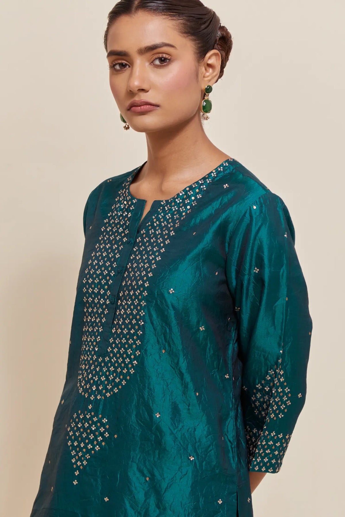 Teal green silk straight short kurta set with hand-embroidered sequins at the neck, borders running along the hem and sleeve edges, and scattered gold sequins embellishments all-over.