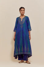 Teal blue silk kurta set with asymmetric hem and hand-embroidered leaf motifs with delicate sequins work at the neck, sleeves, and hem, with sequins border running along the edges.