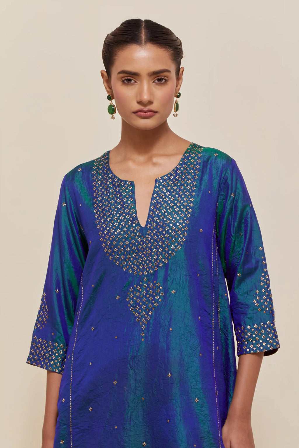 Teal blue silk kurta set with asymmetric hem and hand-embroidered leaf motifs with delicate sequins work at the neck, sleeves, and hem, with sequins border running along the edges.