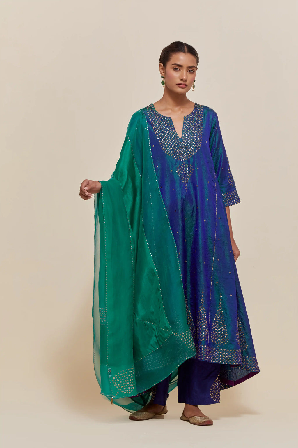 Teal blue silk kurta set with asymmetric hem and hand-embroidered leaf motifs with delicate sequins work at the neck, sleeves, and hem, with sequins border running along the edges.