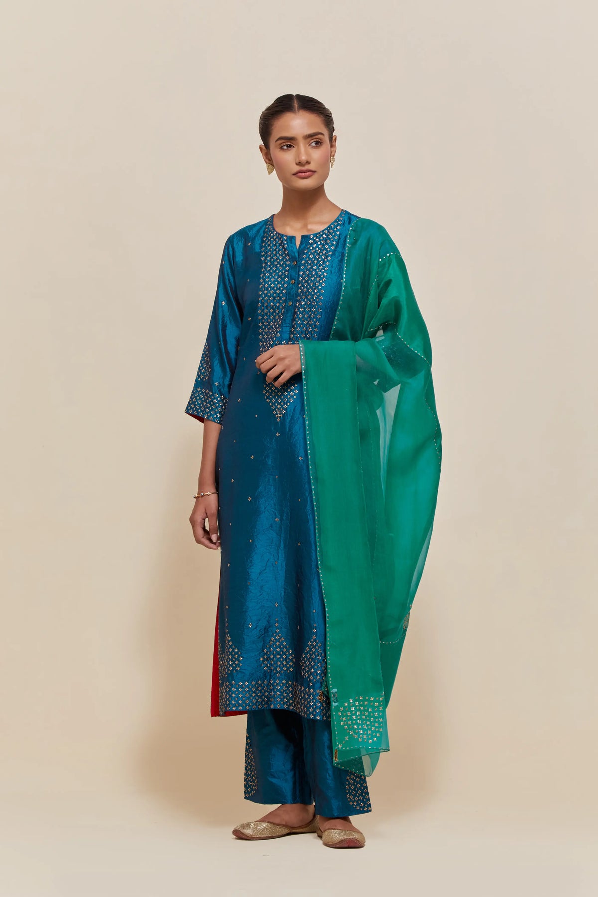 Teal silk straight kurta set with hand-embroidered sequins at the neck, borders running along the hem and sleeve edges, and scattered gold sequins embellishments all-over.