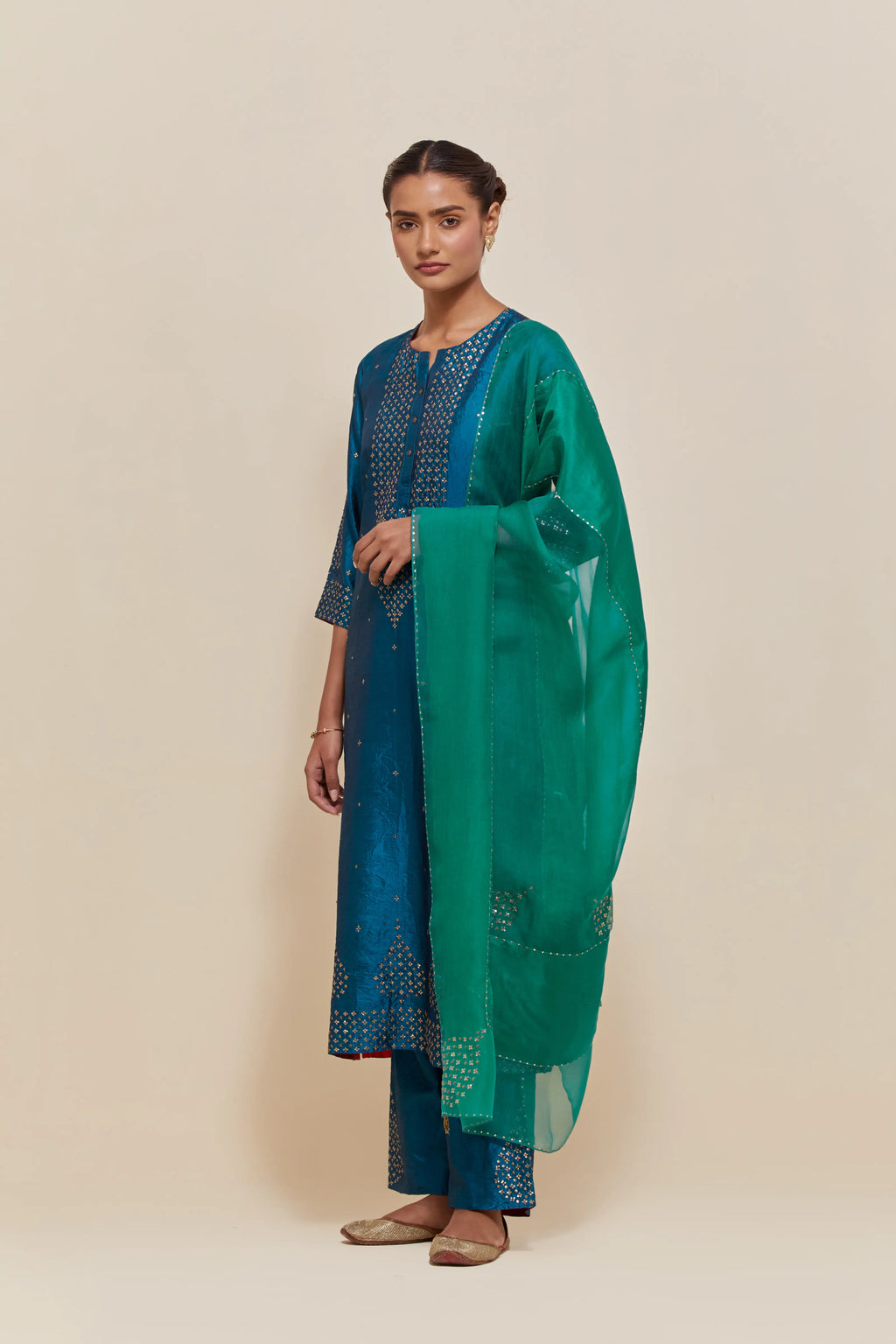 Teal silk straight kurta set with hand-embroidered sequins at the neck, borders running along the hem and sleeve edges, and scattered gold sequins embellishments all-over.