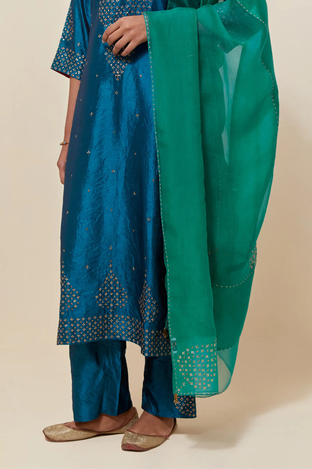 Teal silk straight kurta set with hand-embroidered sequins at the neck, borders running along the hem and sleeve edges, and scattered gold sequins embellishments all-over.