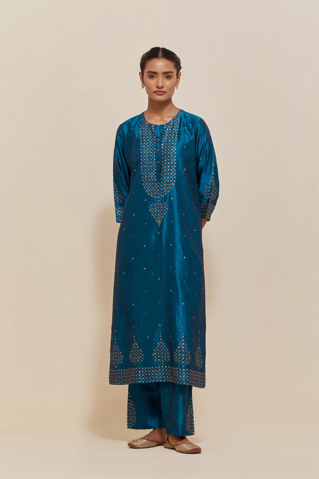 Teal silk straight kurta set with hand-embroidered sequins at the neck, borders running along the hem and sleeve edges, and scattered gold sequins embellishments all-over.