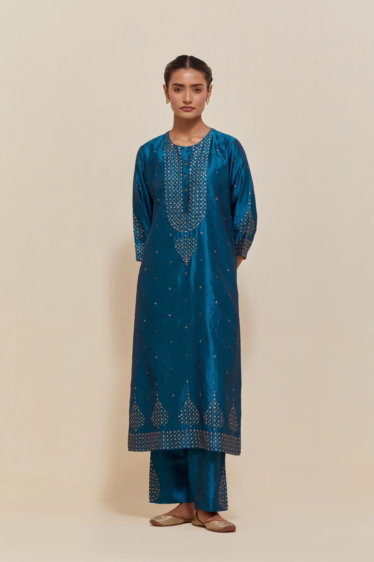 Teal silk straight kurta set with hand-embroidered sequins at the neck, borders running along the hem and sleeve edges, and scattered gold sequins embellishments all-over.