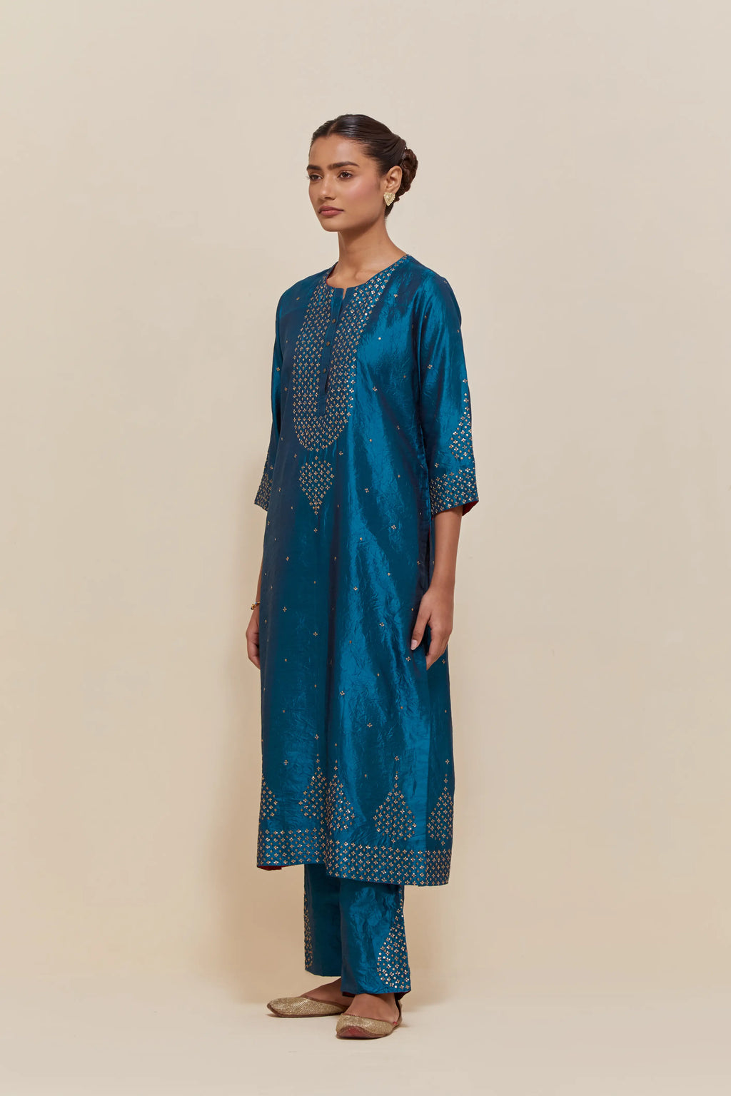 Teal silk straight kurta set with hand-embroidered sequins at the neck, borders running along the hem and sleeve edges, and scattered gold sequins embellishments all-over.