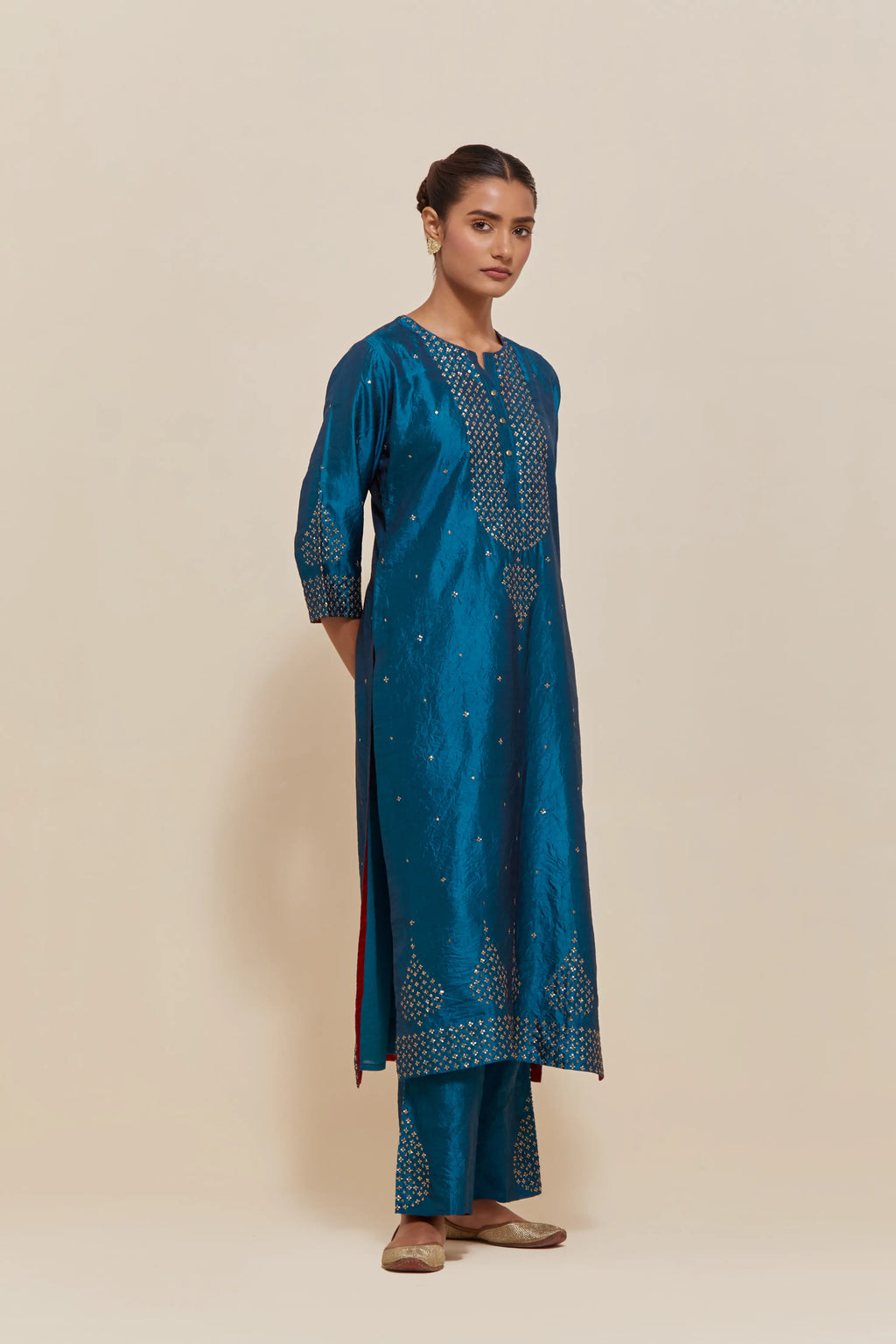 Teal silk straight kurta set with hand-embroidered sequins at the neck, borders running along the hem and sleeve edges, and scattered gold sequins embellishments all-over.