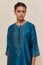 Teal silk straight kurta set with hand-embroidered sequins at the neck, borders running along the hem and sleeve edges, and scattered gold sequins embellishments all-over.