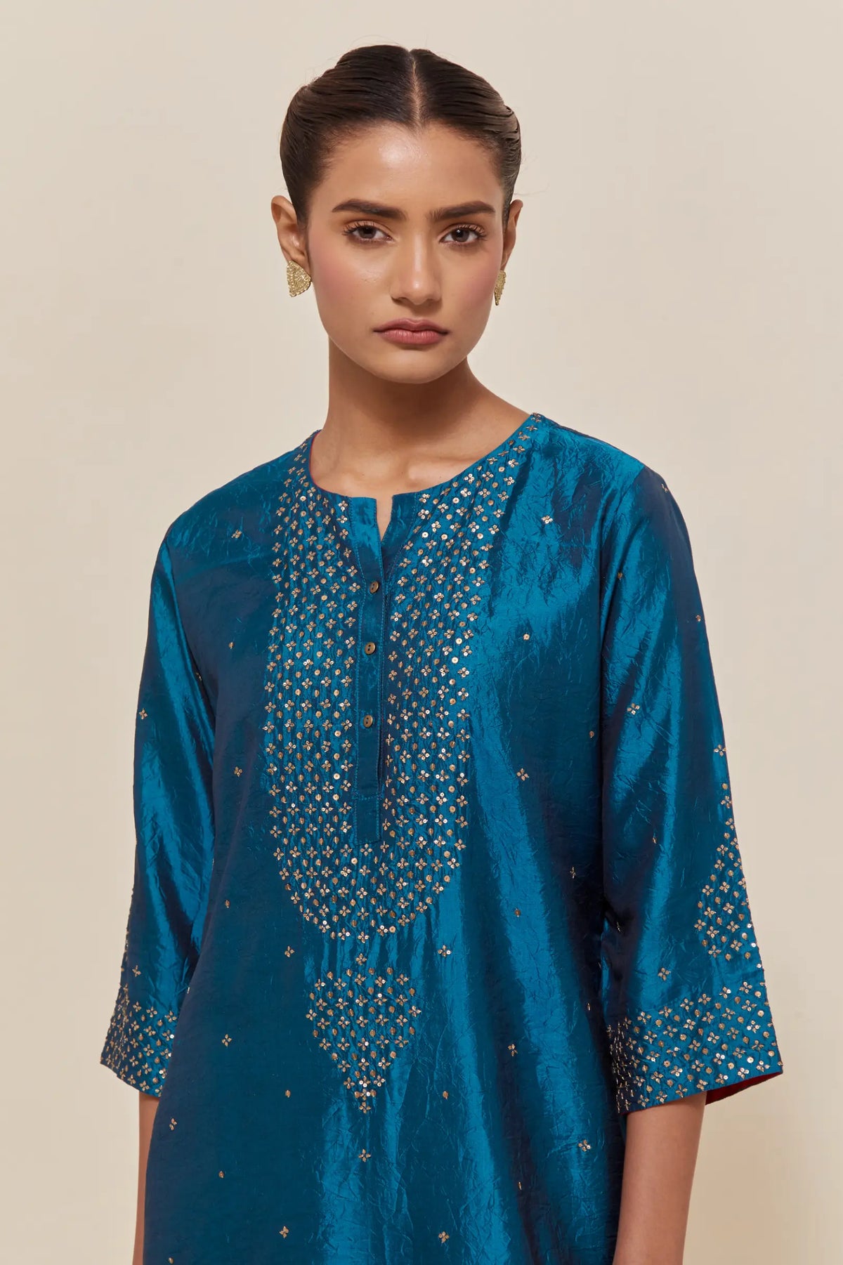 Teal silk straight kurta set with hand-embroidered sequins at the neck, borders running along the hem and sleeve edges, and scattered gold sequins embellishments all-over.