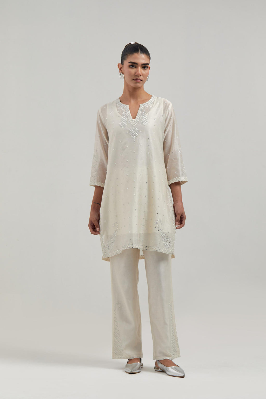 Off white silk Chanderi straight short kurta set with hand-embroidered paisley motifs with delicate mirror and sequins work at neck, hem, and sleeves, with narrow borders along the edges.